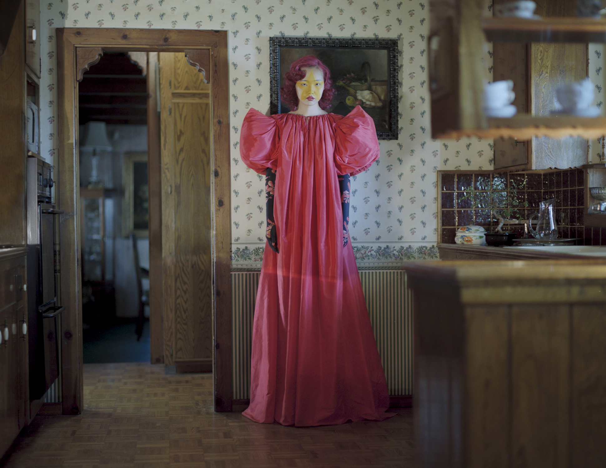 A model with yellow star makeup in a dramatic red cloak standing in a kitchen